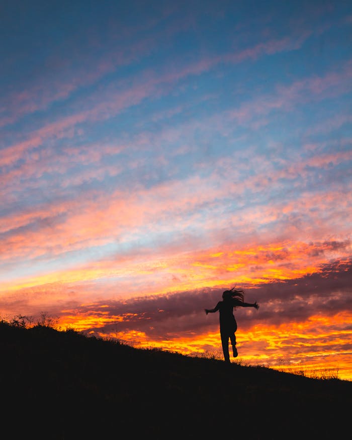An individual dances joyfully against a vibrant, colorful sunset sky.